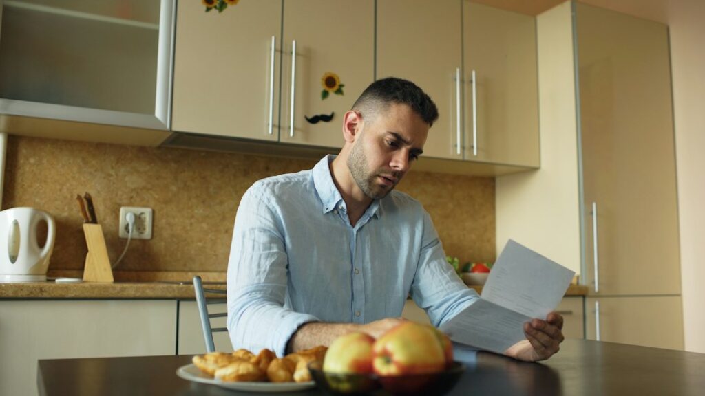 A person reviews a cancellation notice, payment records, and insurance policy documents at a kitchen table.