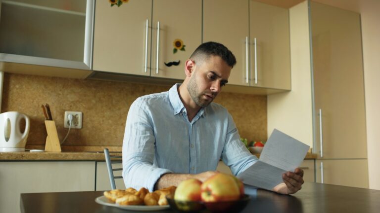 A person reviews a cancellation notice, payment records, and insurance policy documents at a kitchen table.