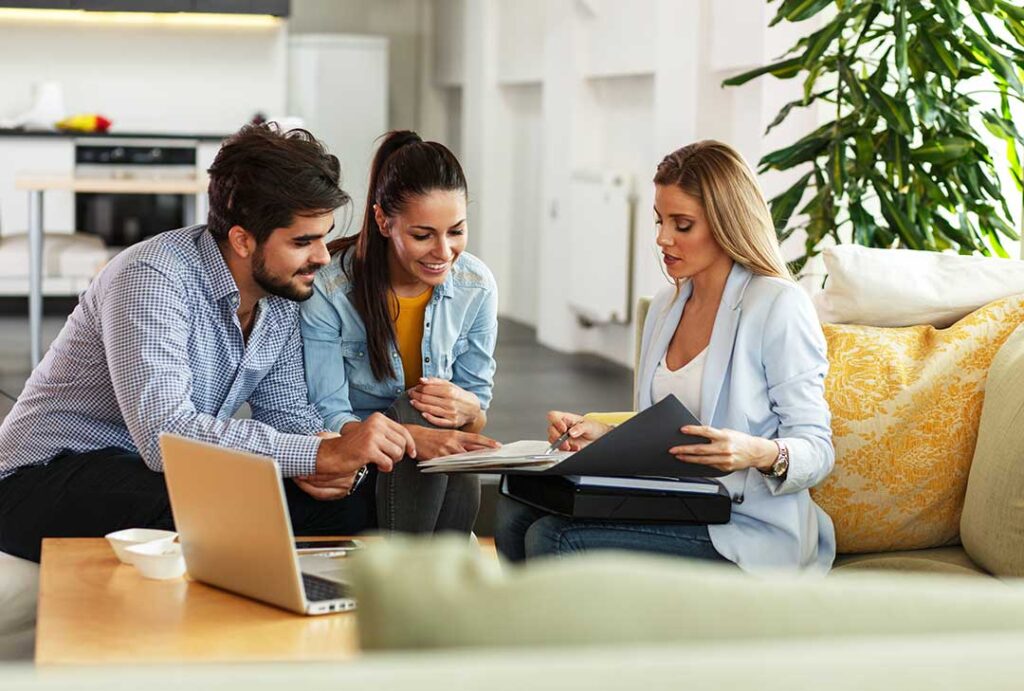 A couple reviews health insurance documents beside a notebook and calculator at a kitchen table.